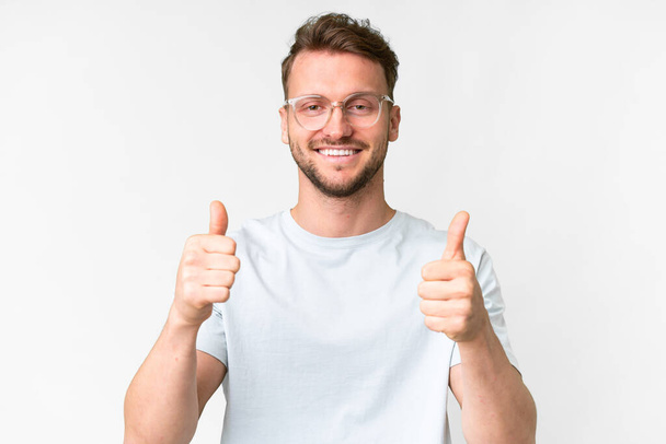 Молодий красивий білий чоловік над ізольованим білим тлом З окулярами і з великим пальцем вгору
 - Фото, зображення