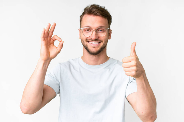 Молодий красивий кавказький чоловік над ізольованим білим тлом З окулярами і роблячи добре знак
 - Фото, зображення