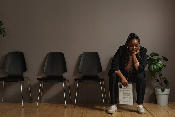 Африканська молода жінка сидить з резюме в залі очікування наодинці і чекає своєї черги в інтерв'ю. - Фото, зображення