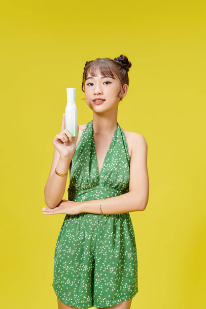 young asian girl in the studio with cosmetics bottle on a yellow background - Фото, изображение