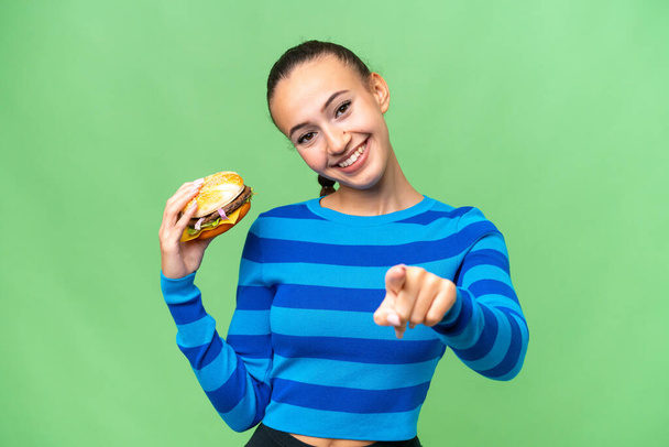 Junge Araberin mit fröhlichem Gesichtsausdruck, die einen Burger vor sich hält - Foto, Bild