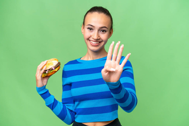 Junge Araberin hält glücklich einen Burger über sich und zählt mit den Fingern vier - Foto, Bild