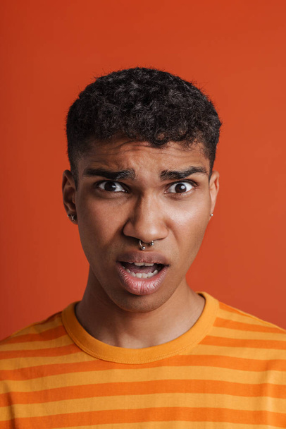 Young black man with piercing expressing surprise at camera isolated over red background - Foto, Bild