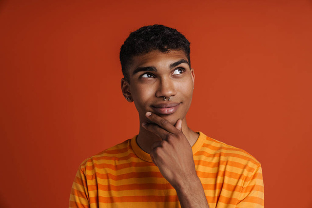 Young black man with piercing smiling and looking aside isolated over red background - Foto, afbeelding