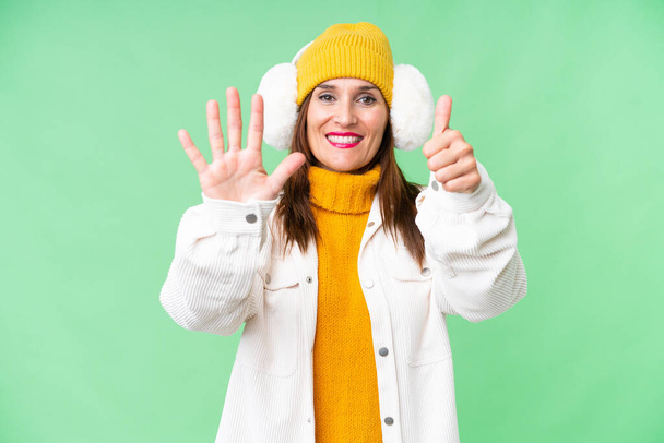 Mujer de mediana edad con manguitos de invierno sobre fondo de croma clave aislado contando seis con los dedos - Foto, imagen