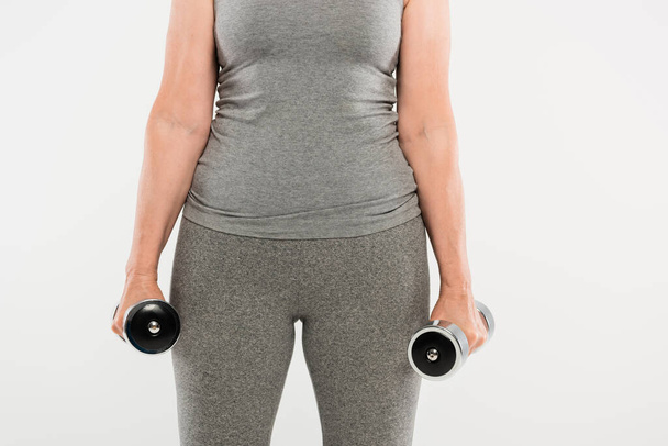cropped view of senior woman in grey sportswear exercising with dumbbells isolated on grey  - Fotografie, Obrázek