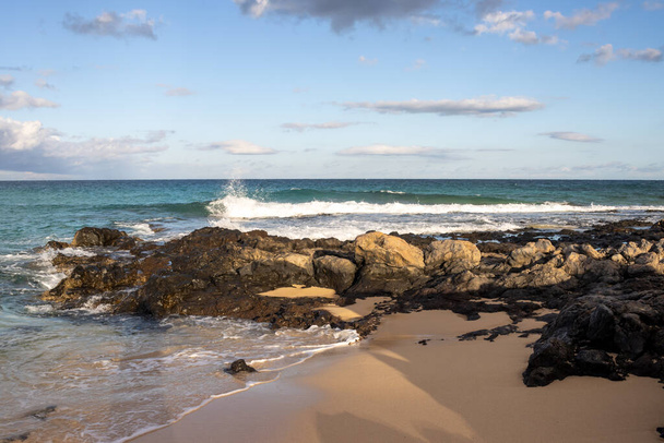 Combination of a sand and rocky coast at the beach of Atlantic ocean. Blue sky with white clouds. Parque Natural Dunas de Corralejo, Fuerteventura, Spain. - Fotó, kép