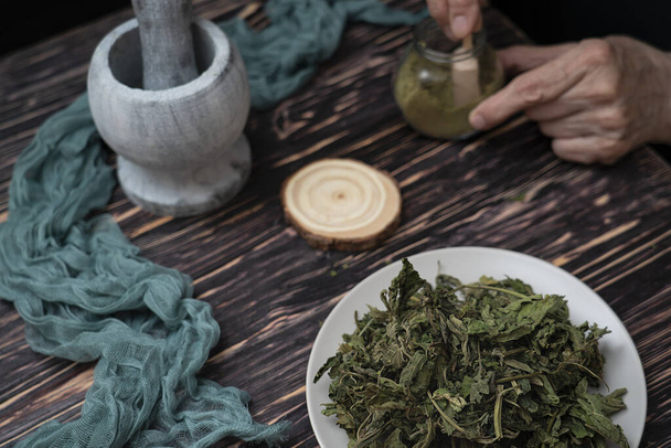Zielarz przygotowuje proszek z suszonych majowych liści pokrzywy. Ludzie, medycyna alternatywna. Wysokiej jakości zdjęcie - Zdjęcie, obraz