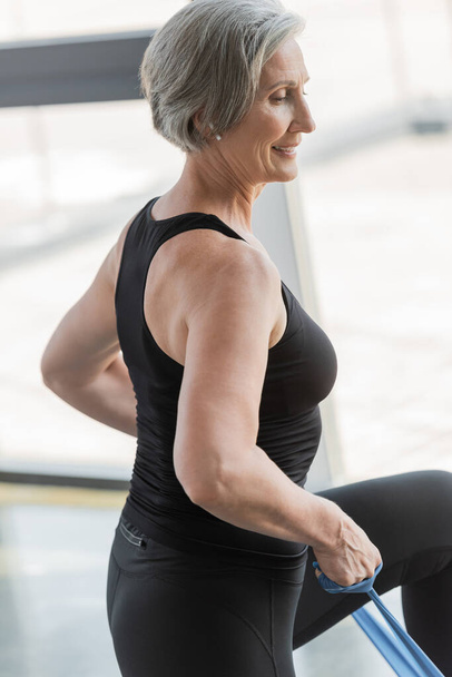 réjoui femme âgée en leggings noirs et débardeur exercice avec des élastiques  - Photo, image