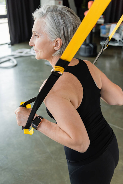 Seniorin in schwarzer Sportbekleidung trainiert mit Federbeinen im Fitnessstudio  - Foto, Bild