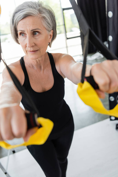 senior woman in black sportswear exercising with suspension straps on blurred foreground  - Fotografie, Obrázek