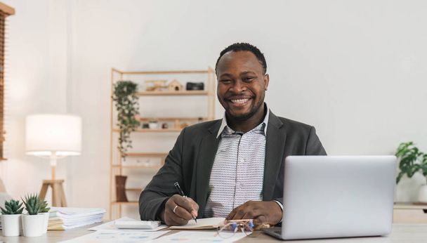konzentriert afrikanisch-amerikanischer Geschäftsmann, der mit Laptop-Dokumenten im Büro arbeitet und Papiere zur Erstellung eines Berichts zur Analyse der Arbeitsergebnisse hält, schwarzer männlicher Analyst, der am Arbeitsplatz am Computer Papierkram erledigt.. - Foto, Bild