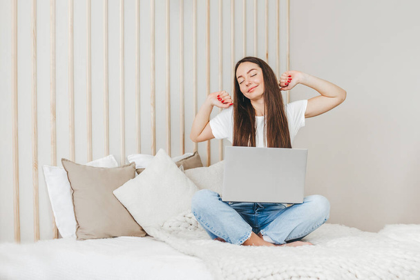 estudiante niña se despertó estiramientos y se sienta con un ordenador portátil en la cama va a trabajar en línea. Trabajo a distancia - Foto, imagen