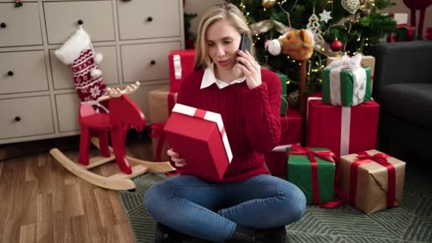 Jovem loira falando no smartphone segurando presente de Natal em casa - Filmagem, Vídeo