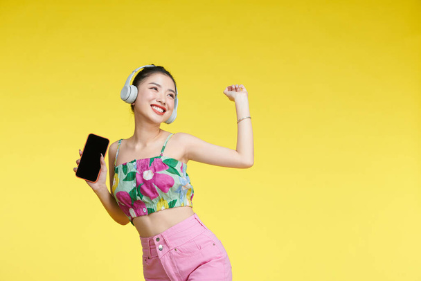 Cute beautiful woman listening to music using wireless headphones isolated over yellow background. - Zdjęcie, obraz