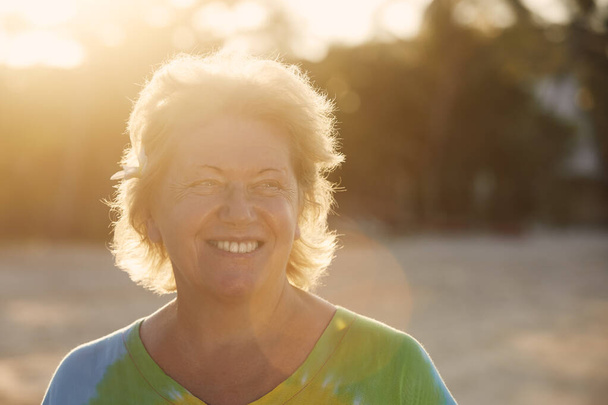Portrait of happy woman on beach in tropical destination at sunset. Senior tourist in tropical destination - Fotografie, Obrázek