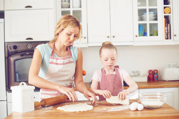 Focused on making something tasty. Cute little girl baking in the kitchen with her mom - Zdjęcie, obraz