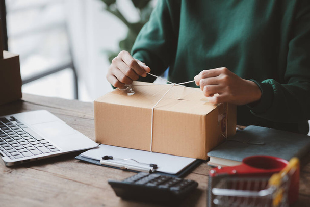 An woman tying a parcel to a customer's box, she owns an online store, she packs and ships through a private transport company. Online selling and online shopping concepts. - Zdjęcie, obraz