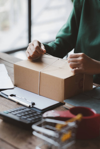 An woman tying a parcel to a customer's box, she owns an online store, she packs and ships through a private transport company. Online selling and online shopping concepts. - Foto, Imagem
