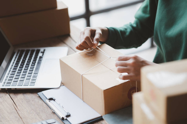 An woman tying a parcel to a customer's box, she owns an online store, she packs and ships through a private transport company. Online selling and online shopping concepts. - Foto, Bild