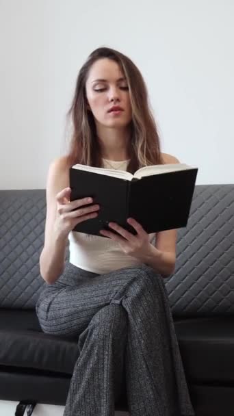 Slim nő ül és olvas egy papírkönyvet. Az olvasás előnyei. Hogyan javíthat az olvasás az életeden? Függőleges videó. - Felvétel, videó