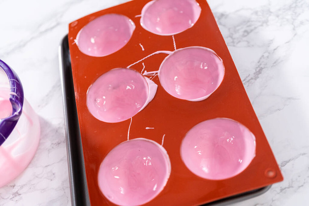 Het vullen van siliconen chocolade mallen met gesmolten roze chocolade om warme chocoladebommen te bereiden. - Foto, afbeelding