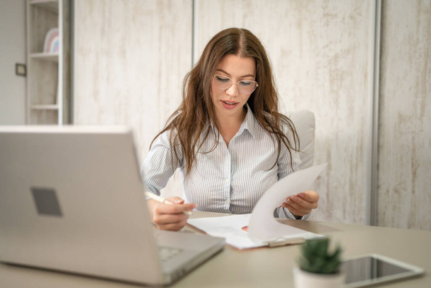 One woman female caucasian entrepreneur businesswoman or secretary sitting at her office at desk work checking paper documents contract wear shirt copy space - Foto, imagen