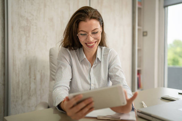 Eine weibliche kaukasische Unternehmerin oder Sekretärin sitzt in ihrem Büro bei der Schreibtischarbeit auf digitalen Tablets für die Online-Suche und trägt Hemdkopierplatz - Foto, Bild
