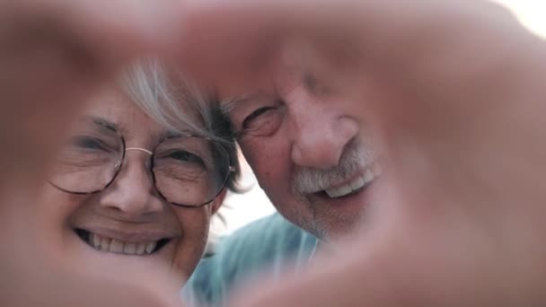 πλάνα από όμορφο ρομαντικό ζευγάρι ηλικιωμένων που δείχνει σχήμα καρδιάς με τα χέρια στην κάμερα - Πλάνα, βίντεο