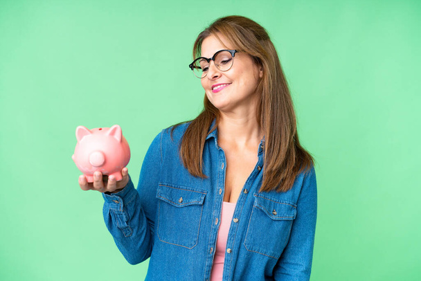 Middle age caucasian woman holding a piggybank over isolated background with happy expression - Photo, Image