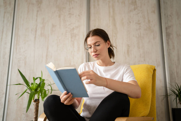 One woman young adult caucasian female sitting in chair at home read book copy space front view real people leisure weekend concept looking to the book thinking contemplate - Fotografie, Obrázek