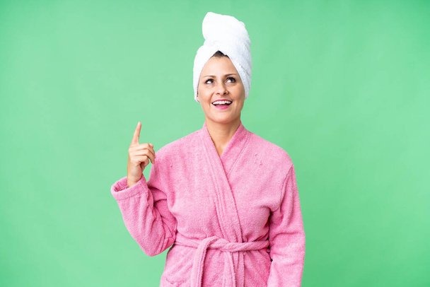 Middle age caucasian woman in a bathrobe over isolated background pointing up and surprised - Foto, afbeelding
