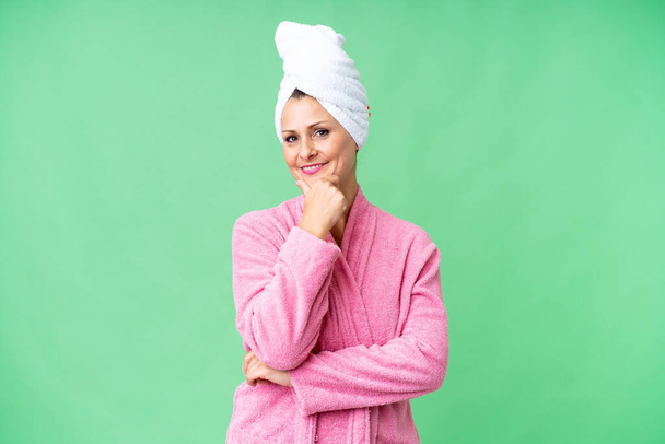 Middelbare leeftijd blanke vrouw in een badjas over geïsoleerde achtergrond glimlachen - Foto, afbeelding