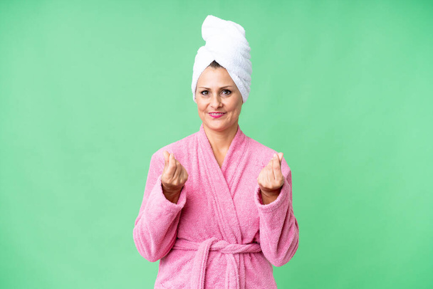 Middle age caucasian woman in a bathrobe over isolated background making money gesture - Photo, Image