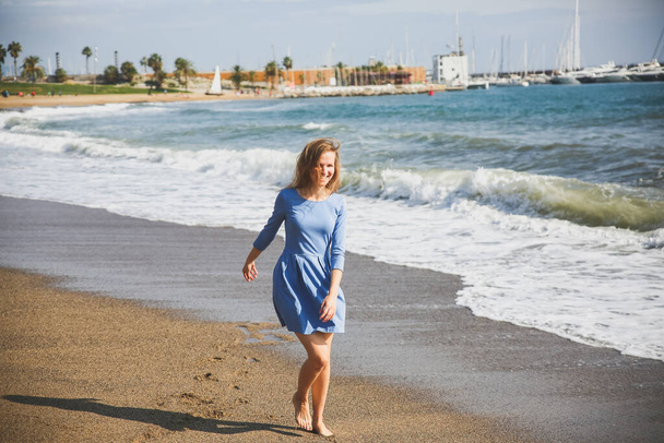 Hermosa chica en vestido azul está caminando por la playa. Increíble foto de verano. Mujer bailando y saltando cerca del mar. Emociones felices y divertidas. Concepto de viaje de vacaciones. Patas delgadas. Agua tibia del océano. - Foto, Imagen