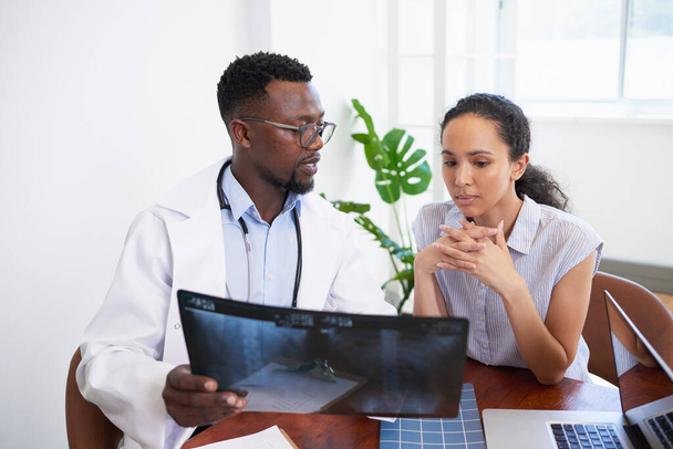 Schwarzer Arzt erklärt jungen besorgten Patienten in Arztpraxis Röntgenergebnisse. Hochwertiges Foto - Foto, Bild