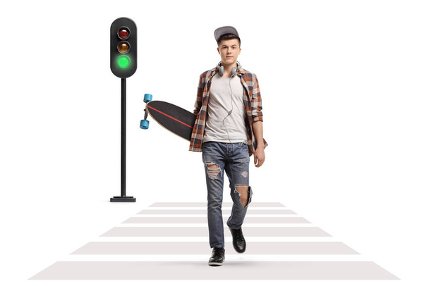 Full length portrait of a male skater with a longboard walking towards the camera at a pedestrian crossing isolated on white background - Fotó, kép