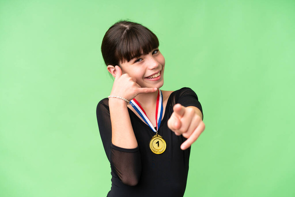 Petite fille caucasienne avec des médailles sur fond isolé faisant geste de téléphone et pointant devant - Photo, image
