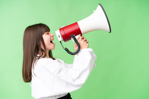 Little Caucasian girl doing karate over isolated background shouting through a megaphone - Foto, Imagen