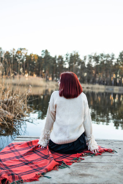 fille est assise sur la jetée et regarde la rivière. parc naturel paisible pendant le coucher du soleil pour un concept de loisirs en plein air serein et relaxant - Photo, image