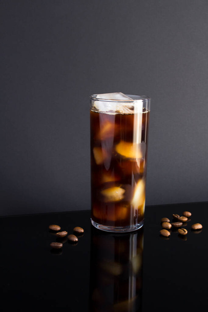 Kalter Brühkaffee mit Eis in einem hohen Glas auf dunklem Hintergrund. Nahaufnahme. Standort vertikal. - Foto, Bild