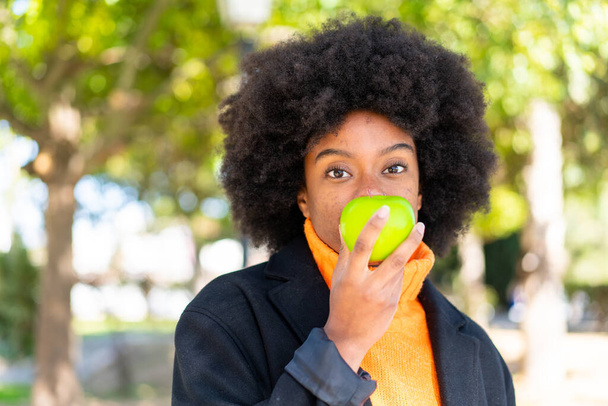 Афроамериканка на улице держит яблоко - Фото, изображение