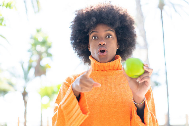 African American girl with an apple at outdoors surprised and pointing front - Фото, зображення