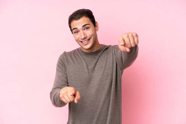 Joven hombre caucásico aislado sobre fondo rosa apuntando frente con expresión feliz - Foto, imagen