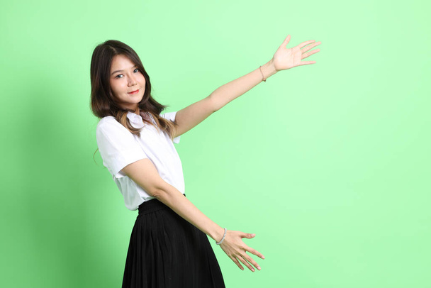 The young school girl with uniform standing on the green background. - Фото, изображение