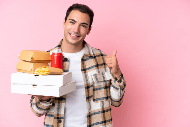 Young caucasian man holding fast food isolated on pink background pointing to the side to present a product - Valokuva, kuva