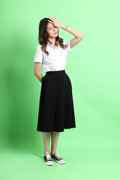 The young school girl with uniform standing on the green background. - Foto, imagen