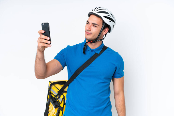 młody biały mężczyzna z termicznym plecakiem odizolowany na białym tle robi selfie - Zdjęcie, obraz