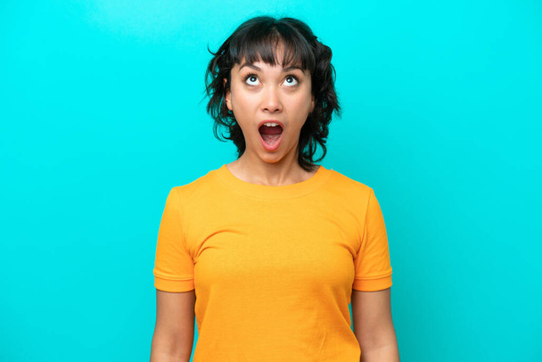 Young Argentinian woman isolated on blue background looking up and with surprised expression - Photo, Image