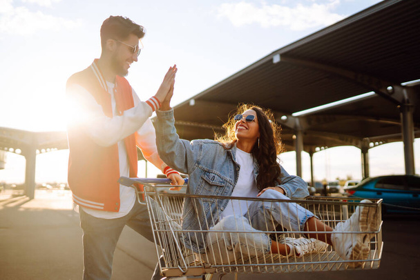  Happy young people racing on shopping cart in summer day with sunlight. Young friends holding mobile phone taking selfie photo using smartphone camera. Selfie time. - Foto, afbeelding